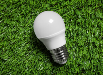 New light bulb on fresh green grass, top view