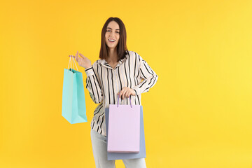 Attractive woman with shop bags on yellow background