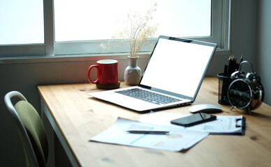 Laptop computer with blank screen, coffee cup, clipboard and pencil holder on wooden desk.
