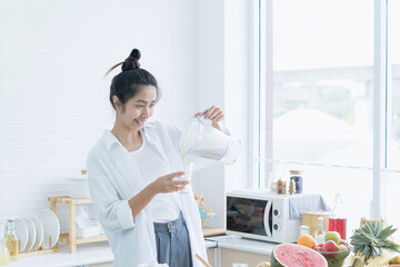 Happy healthy woman pouring vegetable smoothies freshly made from assorted vegetable ingredients in her kitchen.