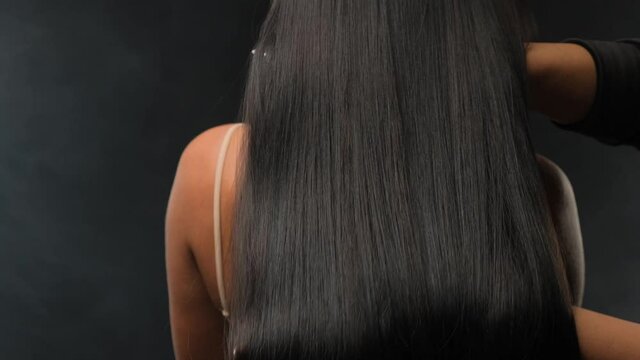 Close-up of a brunette with luxurious hair on a dark background. The girl stands with her back and develops her hair.