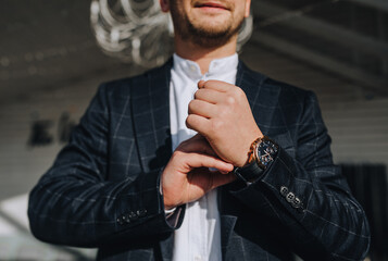 A man, a businessman in a plaid blue suit with a wristwatch, fastens a button on his hand, getting ready for work. - Powered by Adobe