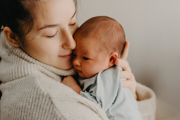 Loving mother carying of her newborn baby at home. Bright portrait of happy mum holding cute infant child on hands. Mother hugging her little 1 months old daughter. - obrazy, fototapety, plakaty