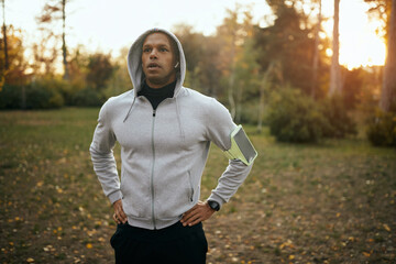 Young African American runner takes break after jogging in park at sunset.