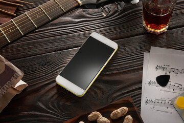 A modern smartphone on a wooden table by a musician with a guitar, notes and a glass of whiskey.
