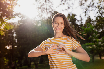 Photo portrait woman spending free time in green city park smiling showing heart sign gesture