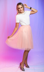 Naklejka premium beautiful woman portrait in studio posing. A girl in a white blouse, a T-shirt and a pink, peach pleated skirt laughs, spins, dances. colored, crimson purple background. holiday, new year, birthday