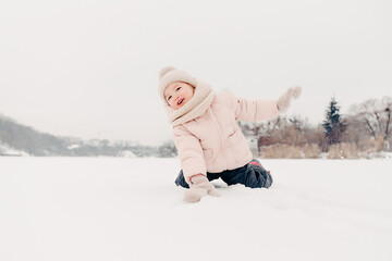 Fototapeta na wymiar Happy laughing girl wearing a pink jacket, scarf and hat, playing in a beautiful snowy winter walk. Girl enjoys winter, frosty day. Playing with snow on winter holidays. Winter holidays concept.