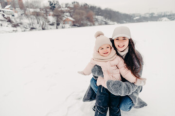 Mom and daughter in winter. Happy family enjoy winter snowy day. They hug, laugh, have fun, ride in the snow and enjoy the winter snowy weather