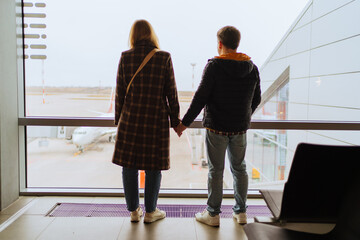 a man and a woman holding hands by the window at the airport. 