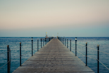 Obraz premium Wooden pier at sunrise in the tropical sea. Palm trees in the distance. Beautiful wooden pier. Long exposure of the sea as a haze