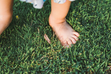 Feet baby child standing on green grass. Girl learn her senses with nature. Kid and sensory concept.