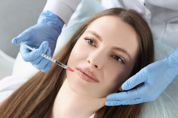 Young woman gets injection of botox in her lips, cosmetologist using syringe