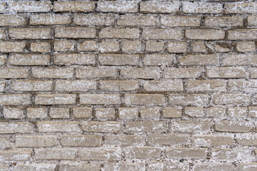 Old wall made of light gray bricks. Weathering, peeling of surface, white cracks.