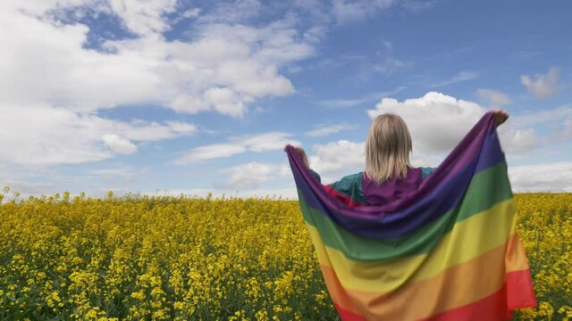 Female with LGBT rainbow flag on yellow rapeseed field in spring