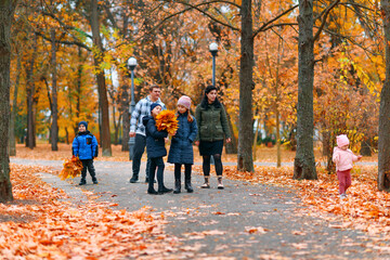 Fototapeta premium Portrait of a family with children in an autumn city park - happy people walking together, beautiful nature with yellow leaves as background.