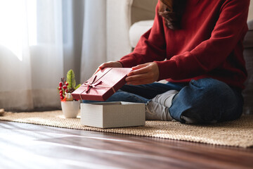 Closeup image of a young woman opening a gift box at home