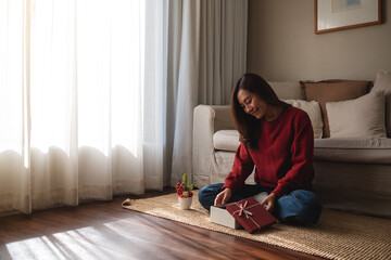 Portrait image of a young asian woman opening a gift box at home - Powered by Adobe