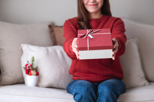 Closeup image of a young woman holding and giving a red present box