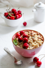 Herculean porridge with hazelnuts, granola and cherry berries in a pink plate o white table. 