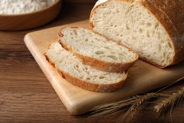 Cut tasty sodawater bread and wheat spikes on wooden table