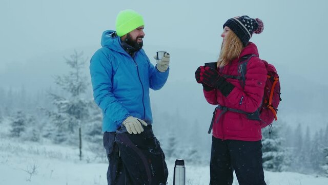 Lviv, Ukraine - January 19, 2021: Cute couple drinking hot coffee or tea stan at winter mountains landscape. Concept of travel and adventure. Hiking outdoors couple relationship. Slow motion