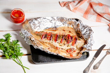 Baked white fish with vegetables in foil on a baking sheet, baked pike perch in foil on white...