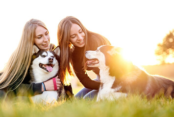 Millennial girls playing with their siberian husky dogs outdoors - Owners and their pets having fun...