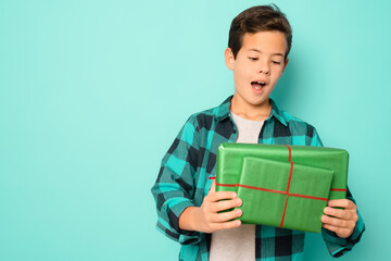 Happy kid boy holding many present and gift boxes isolated over green background.