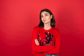Young woman in a christmas sweater on a red background looks thoughtfully into nowhere, a bored indifferent look