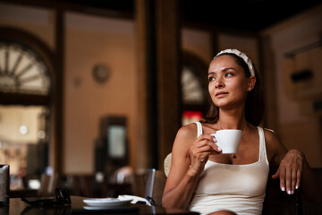 Stylish young woman drinking coffee at cafe. Beautiful girl enjoy in fresh coffee