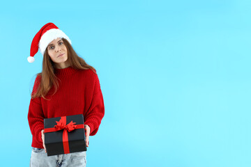Attractive woman in Santa hat holds gift box on blue background