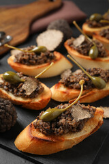 Tasty bruschettas with truffle paste and capers on black table, closeup