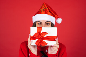 Young woman in a christmas sweater and santa hat on a red background with a gift box in anticipation of the new year