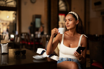 Stylish young woman drinking coffee at cafe. Beautiful girl enjoy in fresh coffee