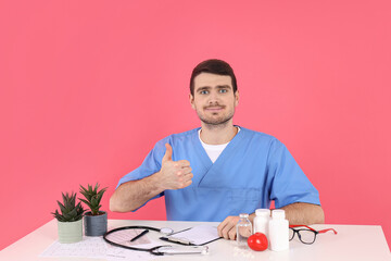 Doctor intern sits at workplace on pink background