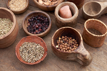 Medieval food in wooden and ceramic dinnerware. Cereals, seeds, dried berries, beans, salt and...