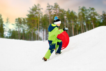 Fototapeta na wymiar childhood, sledging and season concept - happy little boy with snow saucer sled outdoors in winter over snowy forest or park background