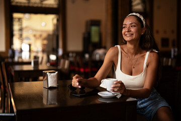 Stylish young woman drinking coffee at cafe. Beautiful girl enjoy in fresh coffee