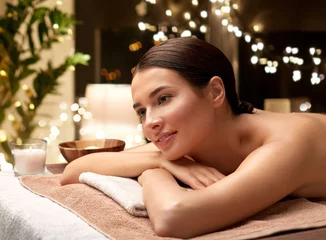 Abwaschbare Fototapete Spa wellness, beauty and relaxation concept - young woman lying at spa or massage parlor over christmas lights on window background