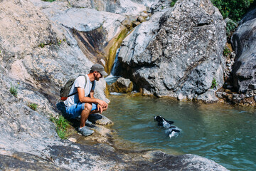 Male owner of spaniel dog walking against mountains and waterfall background.