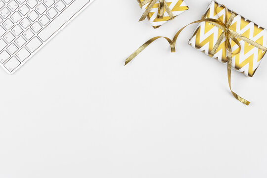 Christmas Presents Wrapped In Golden Paper With Geometric Print, Keyboard On White Background. Business Concept. Freelancer Work Desk. Minimal Festive Composition. Birthday Or Anniversary Gifts.