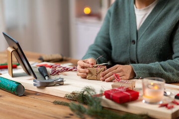 winter holidays and hobby concept - close up of woman with tablet pc computer packing christmas gift or making advent calendar at home