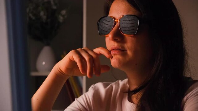 A woman in perforated glasses looks at the computer screen.