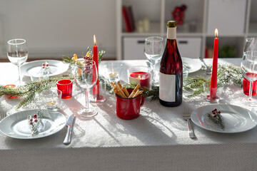 winter holidays, dinner party and celebration concept - christmas table serving with candles, crockery and wine at home