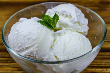 Glass bowl with ice cream balls and mint leaf on a wooden table