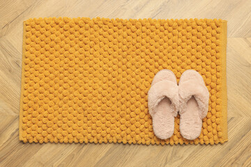 Soft orange bath mat and slippers on floor, top view