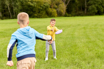 childhood, leisure and people concept - happy boys playing game with flying disc at park