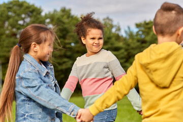 childhood, leisure and people concept - group of happy kids playing round dance at park