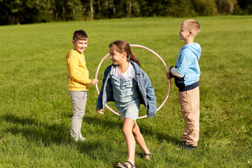childhood, leisure and people concept - group of happy children playing game with hula hoop at park